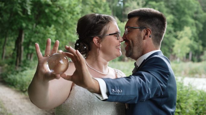 Brautpaar lächelt sich an, während die Braut eine Glaskugel in der Hand hält.